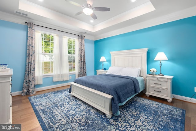 bedroom with a raised ceiling, ornamental molding, wood finished floors, and visible vents