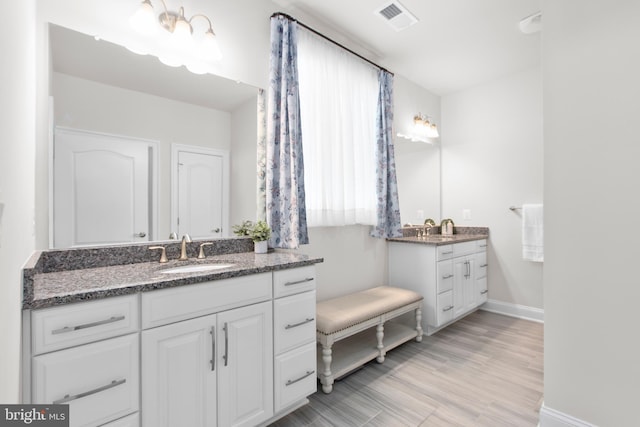 full bath with visible vents, wood finished floors, baseboards, two vanities, and a sink