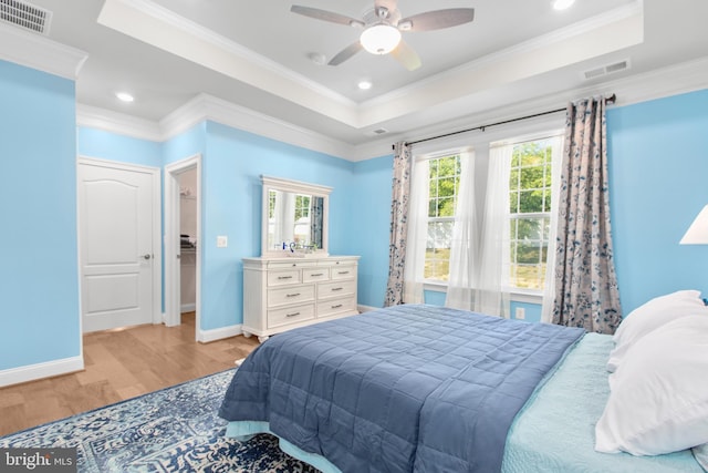 bedroom featuring crown molding, a raised ceiling, light wood-style flooring, and visible vents