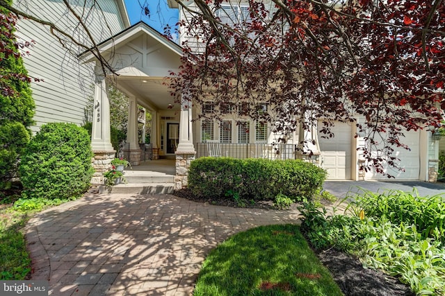 obstructed view of property with covered porch, a garage, and stone siding