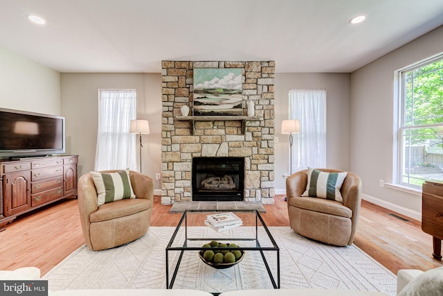 living area with light wood-type flooring, baseboards, a stone fireplace, and recessed lighting