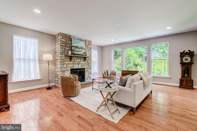 living room with baseboards, light wood-style flooring, a stone fireplace, and recessed lighting
