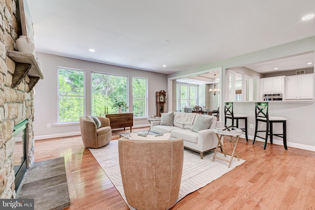living room featuring a fireplace, a chandelier, light wood finished floors, baseboards, and recessed lighting