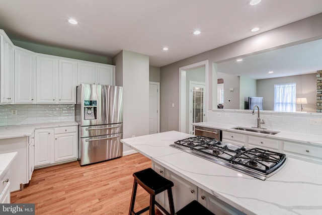 kitchen featuring appliances with stainless steel finishes, a sink, light wood-type flooring, backsplash, and recessed lighting