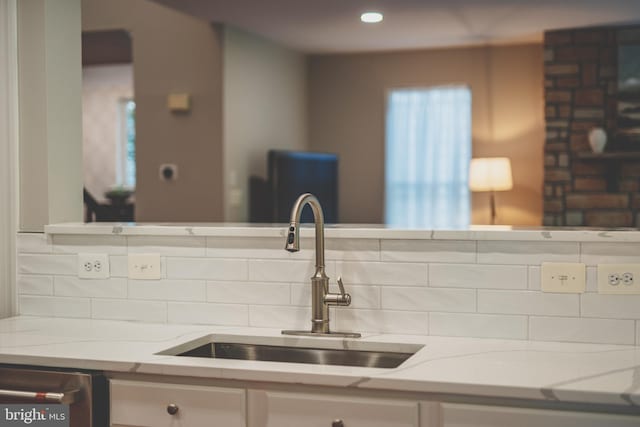 kitchen with a sink, backsplash, dishwasher, and light stone countertops