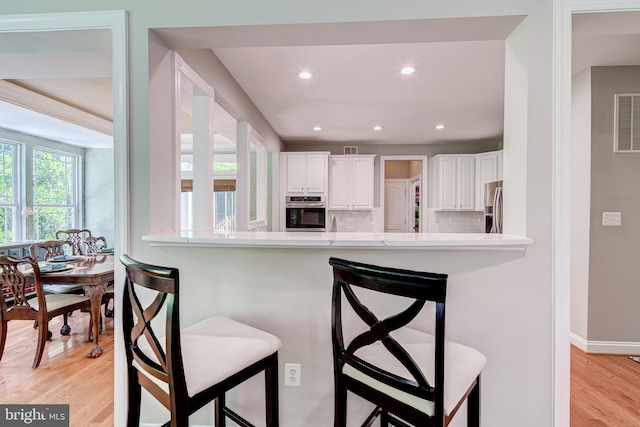 kitchen featuring appliances with stainless steel finishes, white cabinetry, a kitchen breakfast bar, light countertops, and light wood-type flooring