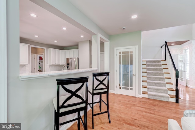 kitchen featuring stainless steel refrigerator with ice dispenser, a breakfast bar, white cabinetry, light countertops, and recessed lighting