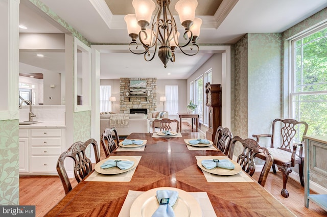 dining area with light wood-type flooring, plenty of natural light, a stone fireplace, wallpapered walls, and a chandelier