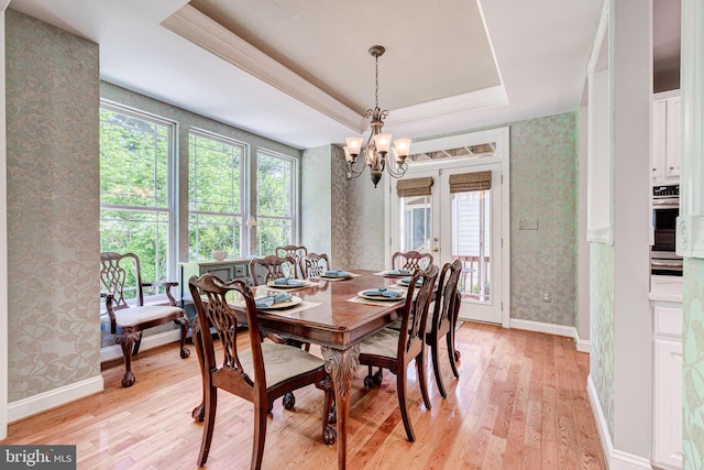 dining space with wallpapered walls, light wood-type flooring, a chandelier, a raised ceiling, and plenty of natural light