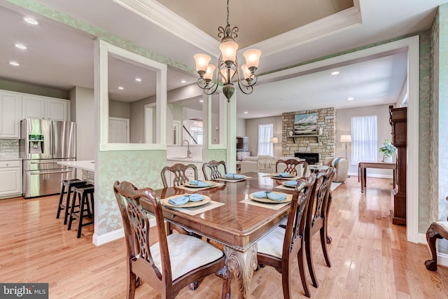 dining room with light wood finished floors, healthy amount of natural light, a stone fireplace, crown molding, and recessed lighting