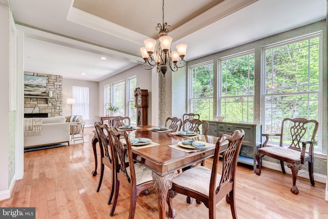 dining space featuring light wood finished floors, a chandelier, a stone fireplace, baseboards, and ornamental molding
