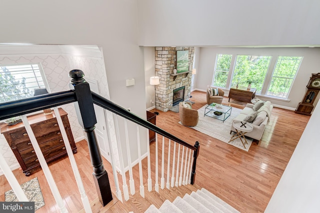 living area featuring wood finished floors, a stone fireplace, baseboards, and stairway
