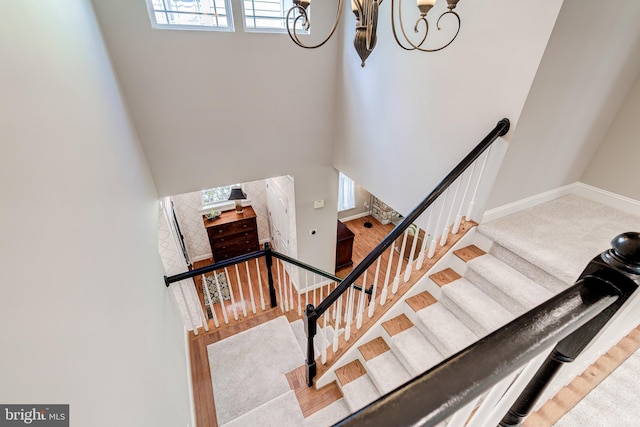 stairs with a chandelier, a high ceiling, baseboards, and carpet flooring