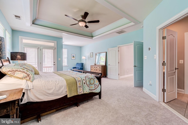 bedroom with multiple windows, a tray ceiling, light colored carpet, and access to outside