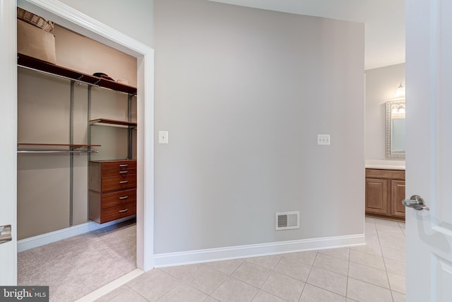 unfurnished bedroom featuring a closet, light tile patterned floors, baseboards, and ensuite bath