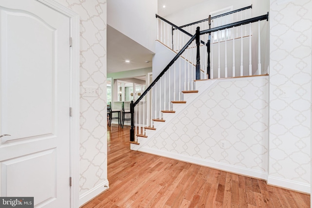 stairway with wood finished floors, baseboards, and wallpapered walls