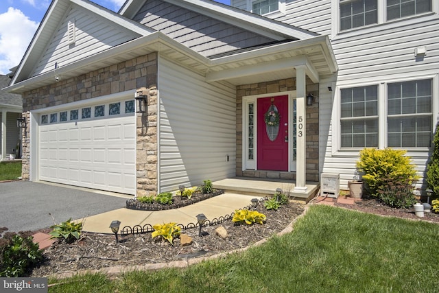 view of exterior entry featuring an attached garage, aphalt driveway, and stone siding