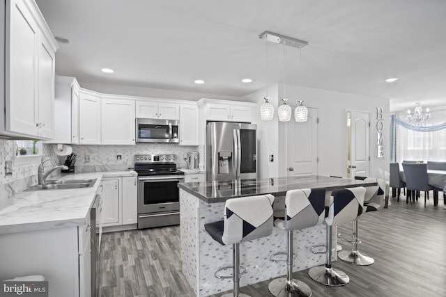 kitchen with appliances with stainless steel finishes, a sink, light wood finished floors, and a kitchen bar