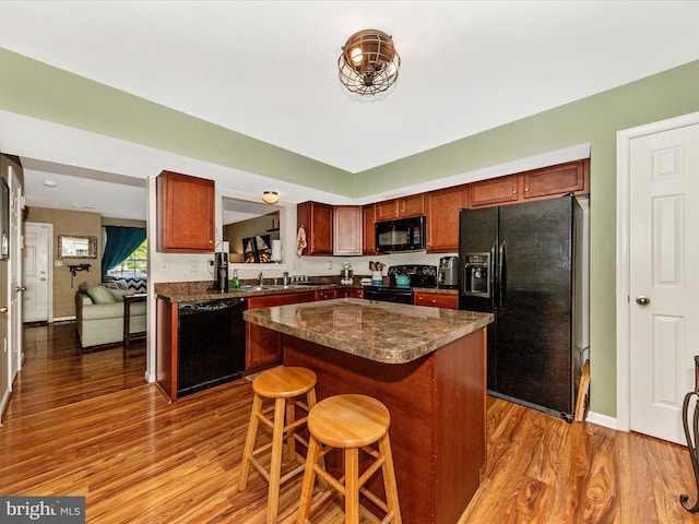 kitchen with a center island, black appliances, dark wood-style flooring, and dark countertops