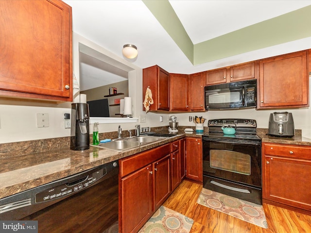 kitchen featuring black appliances, dark countertops, light wood-style flooring, and a sink