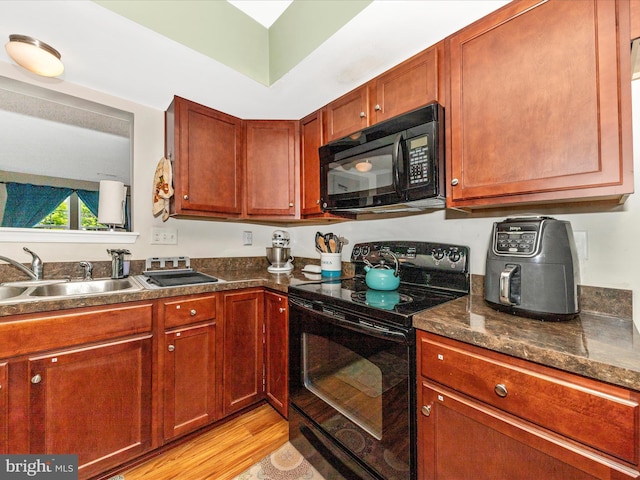 kitchen with a sink, black appliances, dark countertops, and light wood-style flooring
