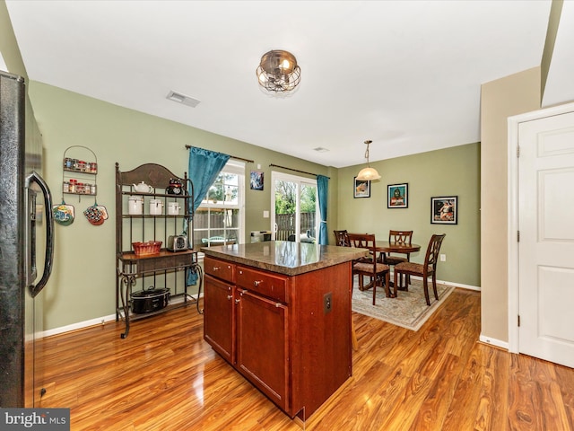 kitchen with black fridge with ice dispenser, light wood-style flooring, dark countertops, visible vents, and baseboards