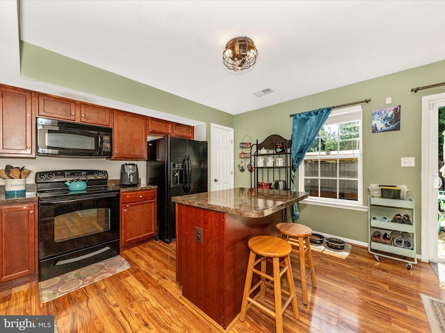 kitchen with black appliances, visible vents, light wood-type flooring, and a breakfast bar area