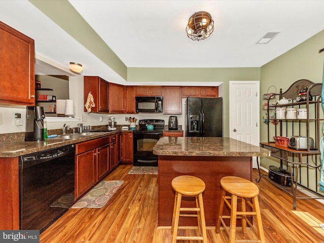 kitchen featuring black appliances, wood finished floors, visible vents, and a sink