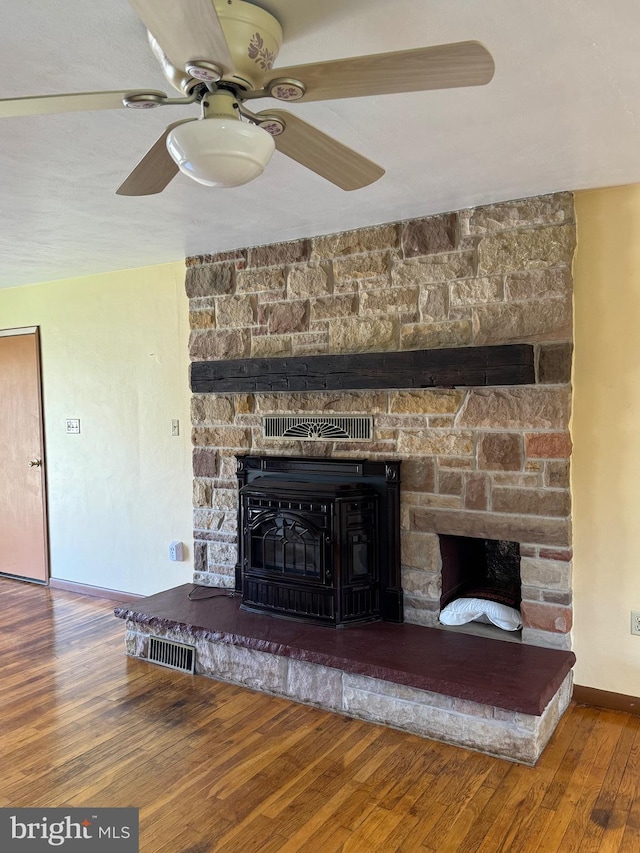 room details with a stone fireplace, ceiling fan, wood finished floors, and visible vents
