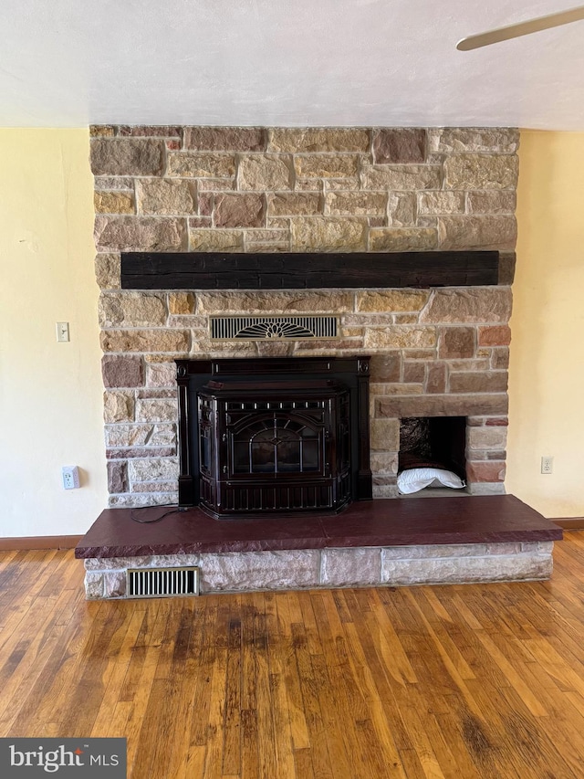room details featuring baseboards, visible vents, wood finished floors, and a stone fireplace