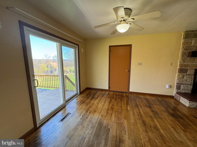 spare room featuring visible vents, hardwood / wood-style flooring, a stone fireplace, and baseboards