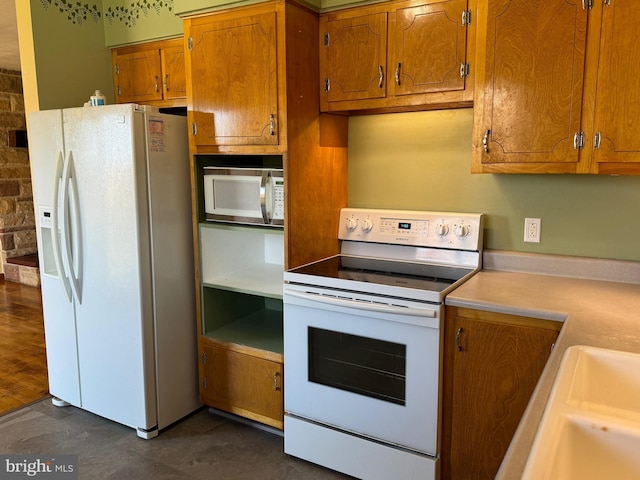 kitchen featuring a sink, white appliances, light countertops, and brown cabinets