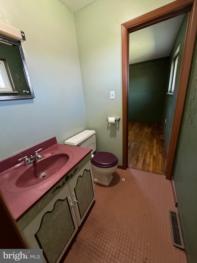 half bath with toilet, visible vents, vanity, and tile patterned flooring