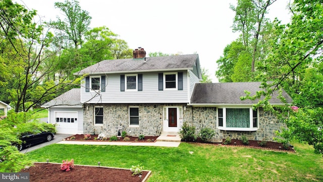 colonial-style house with a front yard, a chimney, stone siding, and a garage
