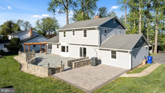 back of house featuring a chimney, roof with shingles, a lawn, central air condition unit, and a patio
