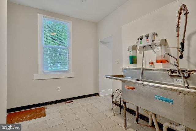 clothes washing area featuring light tile patterned flooring, baseboards, and a sink