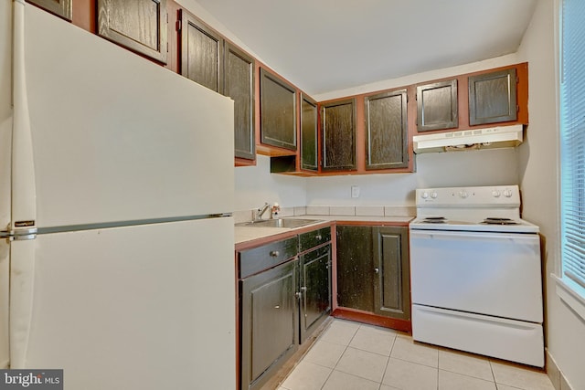 kitchen with a sink, white appliances, light countertops, light tile patterned floors, and under cabinet range hood