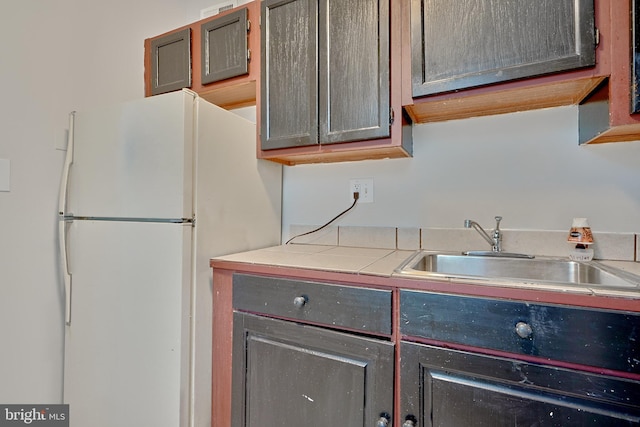kitchen featuring freestanding refrigerator, tile counters, and a sink