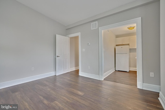 unfurnished bedroom featuring baseboards, freestanding refrigerator, dark wood finished floors, and visible vents