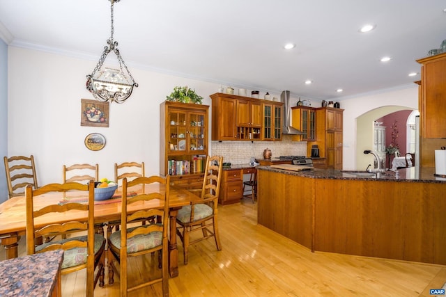 kitchen with arched walkways, wall chimney exhaust hood, brown cabinets, and ornamental molding