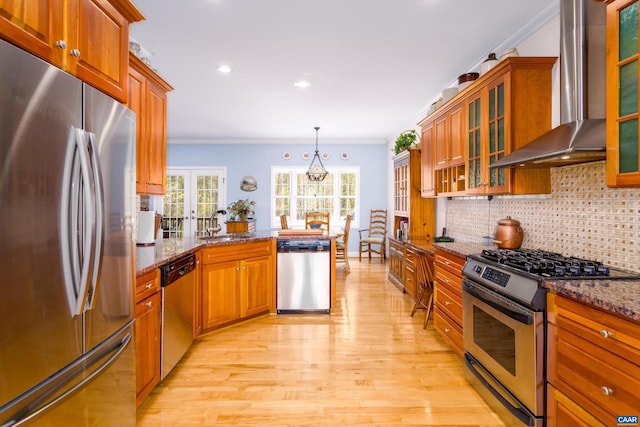 kitchen featuring wall chimney range hood, appliances with stainless steel finishes, light wood-type flooring, a peninsula, and ornamental molding