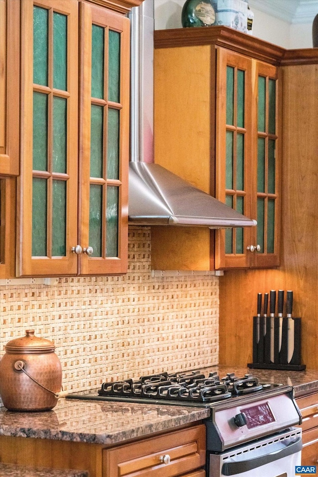 kitchen with wall chimney range hood, backsplash, stainless steel range with gas stovetop, and brown cabinetry