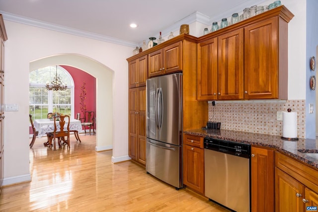 kitchen with arched walkways, brown cabinetry, light wood-style flooring, stainless steel appliances, and backsplash