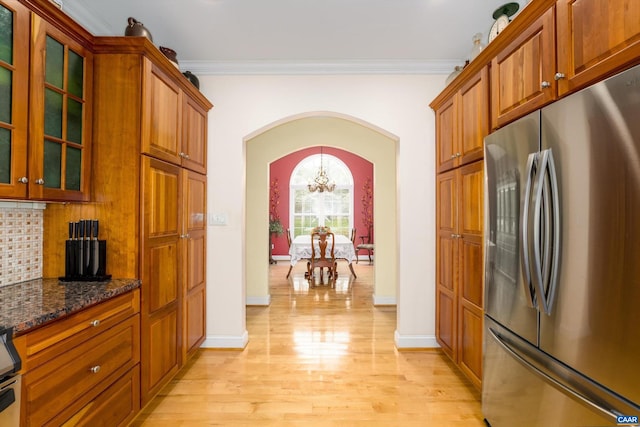 kitchen featuring arched walkways, light wood-type flooring, freestanding refrigerator, glass insert cabinets, and dark stone counters