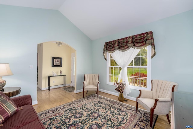living area featuring baseboards, arched walkways, light wood finished floors, and lofted ceiling