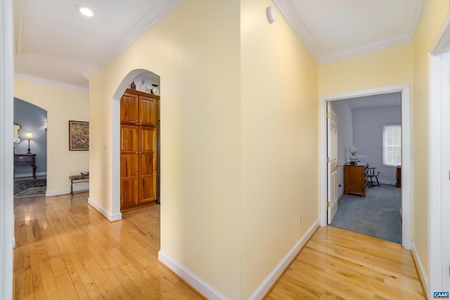 hallway with crown molding, arched walkways, light wood-style flooring, and baseboards