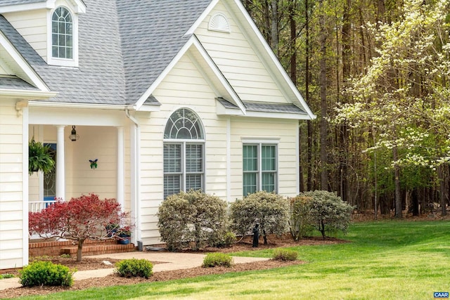 view of side of home featuring a lawn and a shingled roof