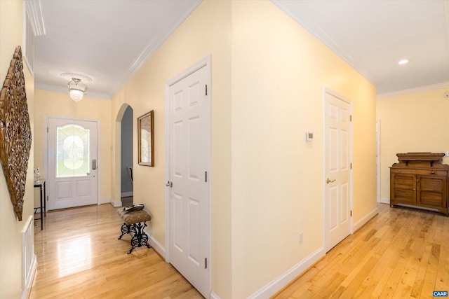 hallway featuring light wood-style floors, arched walkways, baseboards, and ornamental molding