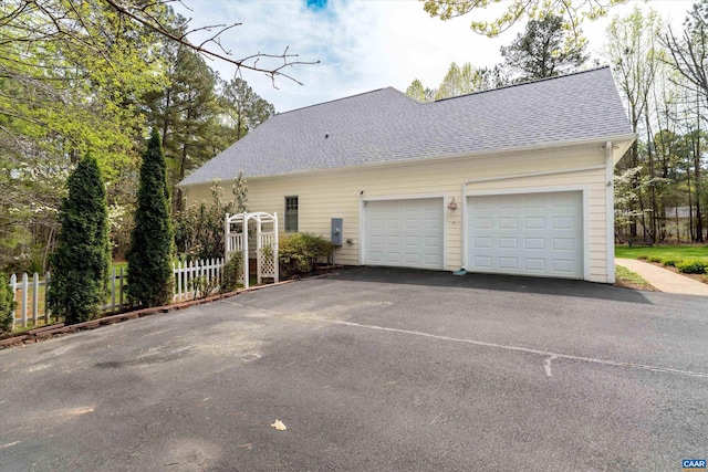 exterior space featuring fence, a shingled roof, an attached garage, and aphalt driveway