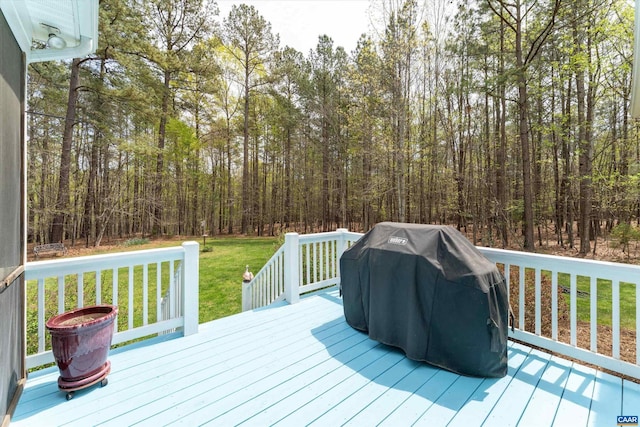 wooden terrace with a lawn, a view of trees, and grilling area